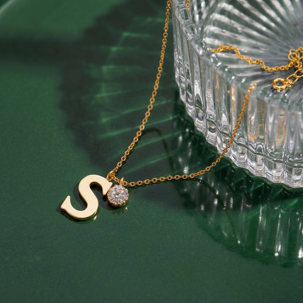 Gold necklace with a letter 'S' pendant on a green surface