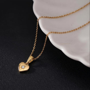 Gold heart-shaped necklace with a diamond pendant on a dark surface.