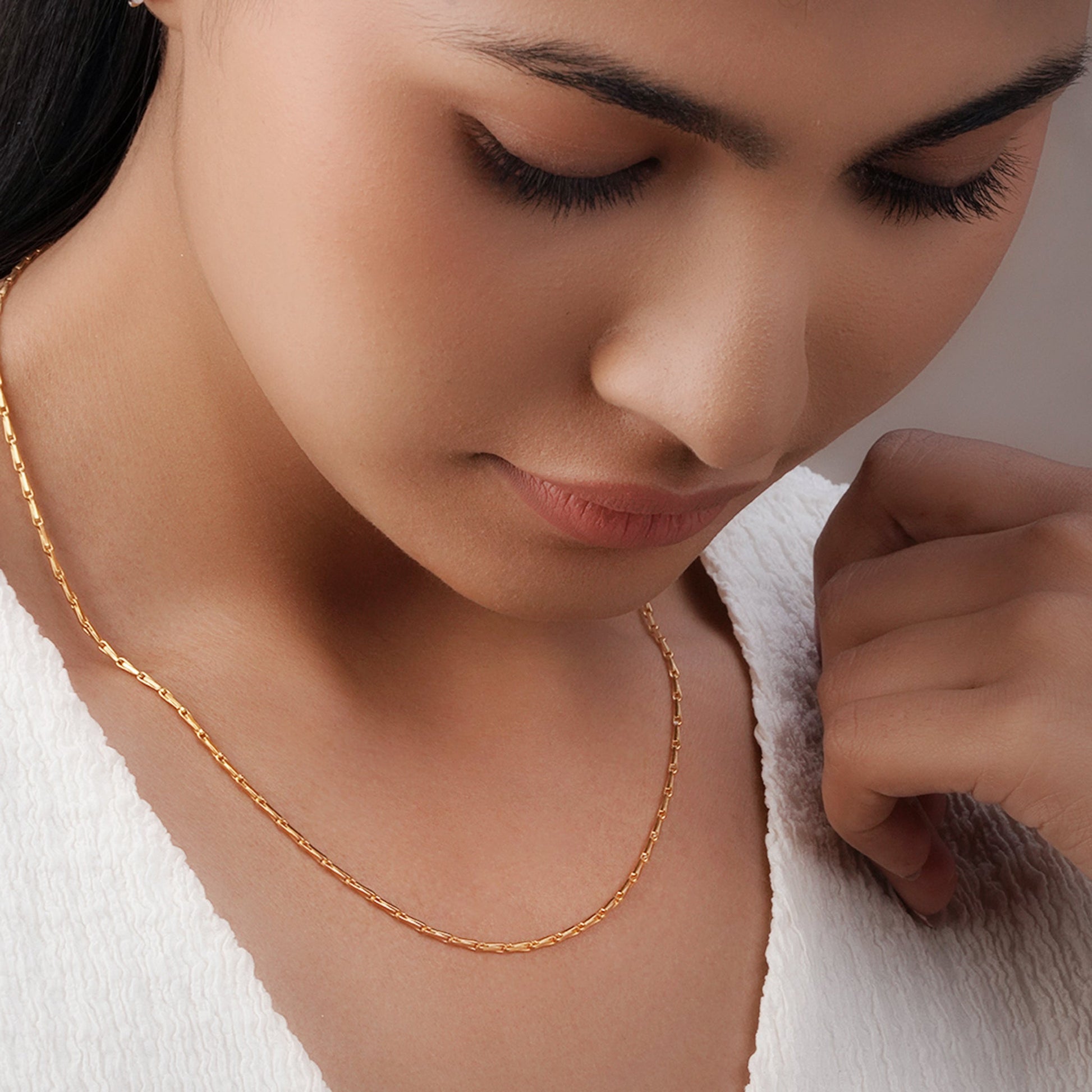 Close-up of a woman wearing a gold polish chain against a neutral background