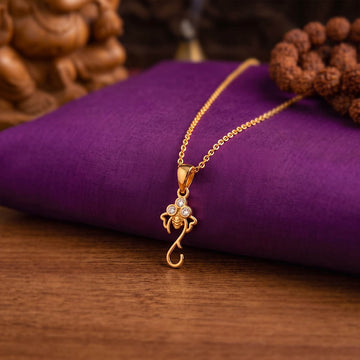 A gold pendant necklace with a small beehive charm set with clear stones, resting on a purple fabric cushion over a wooden surface.