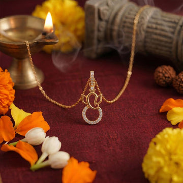 Gold necklace with a pendant on a maroon fabric background with flowers and a lamp.
