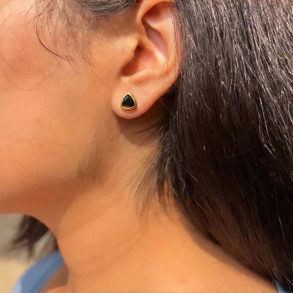 Close-up of an ear wearing a black triangle earring with a blurred background