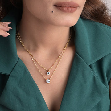 Close-up of a woman wearing a gold necklace with two diamond pendants against a teal background.