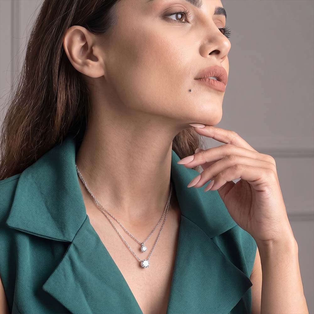 Woman wearing a green top and silver necklaces, with a neutral background