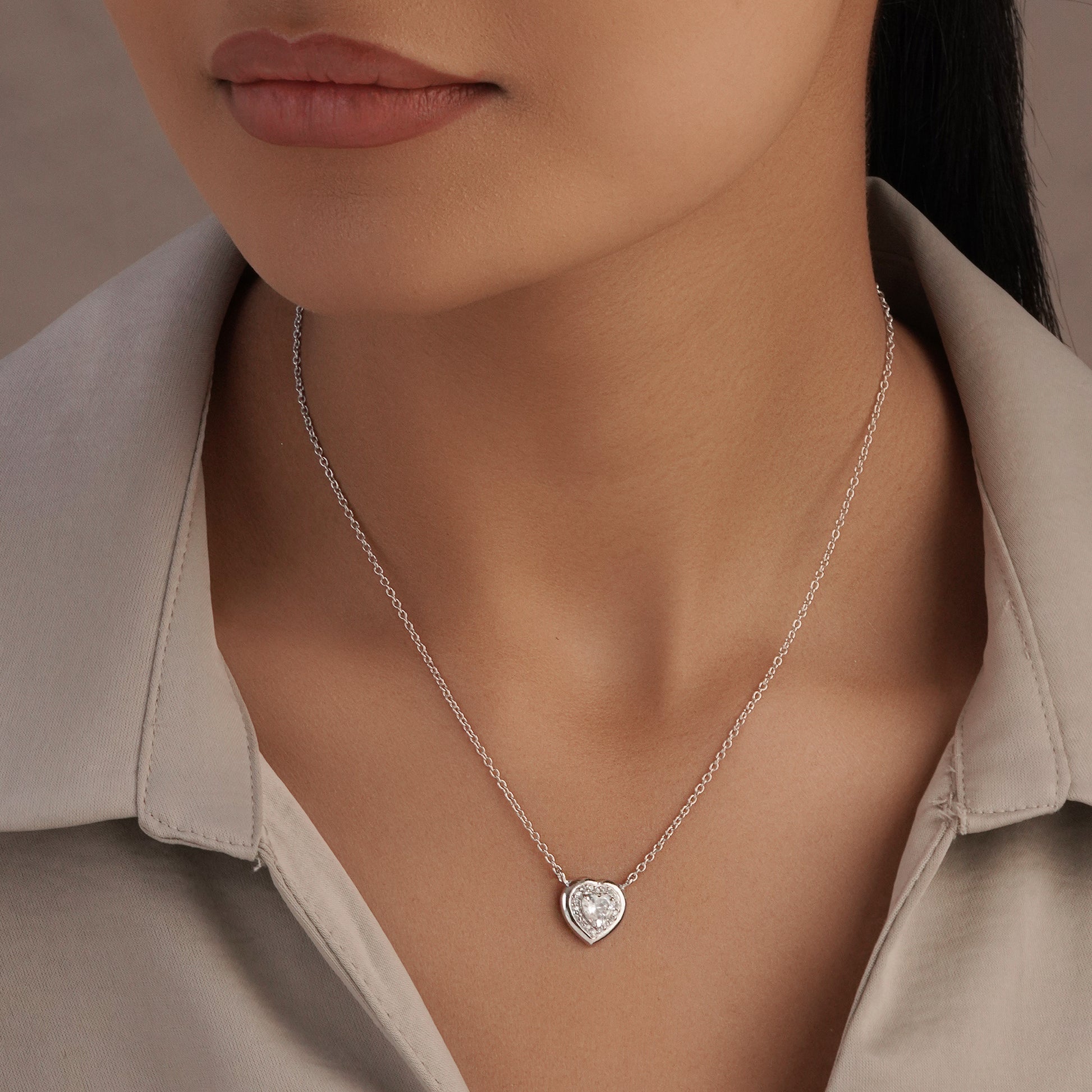 Close-up of a person wearing a silver necklace with a heart-shaped pendant.