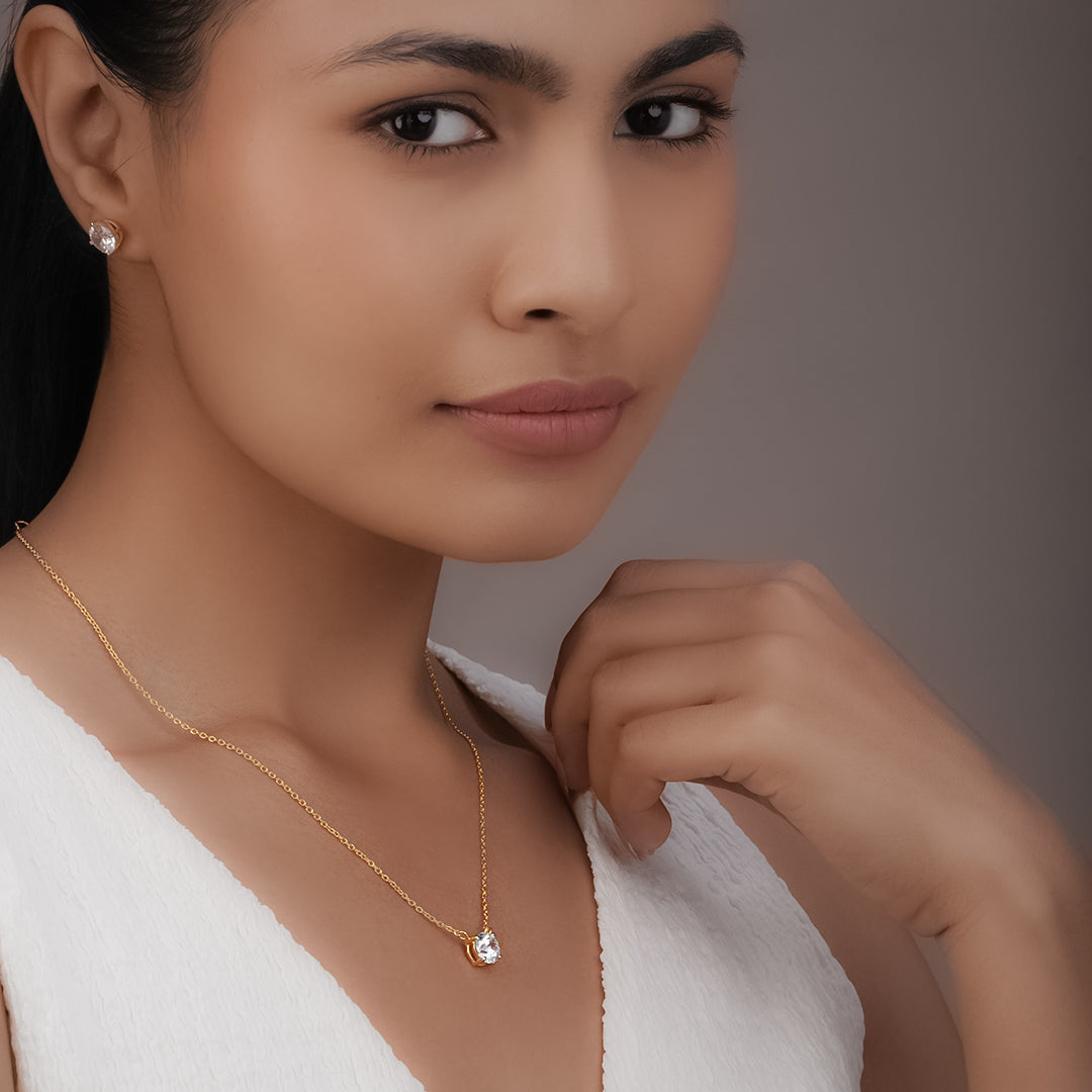 Woman wearing a gold necklace and earrings against a neutral background